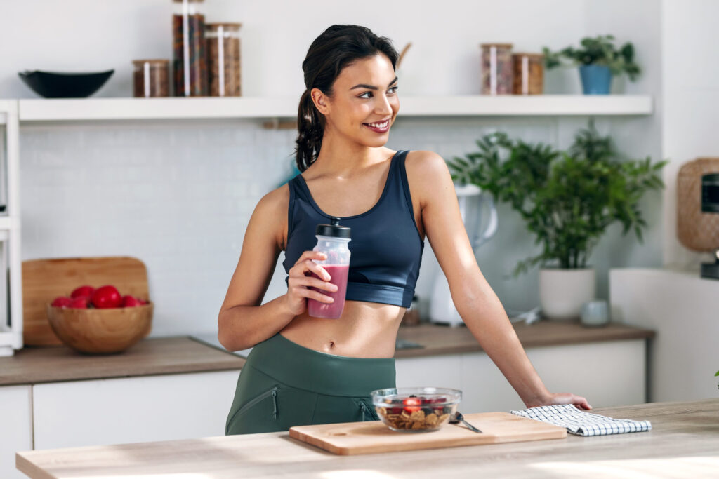 Fehérje edzés után: sportos nő protein shake-et iszik otthon a konyhában az izomregeneráció támogatására
